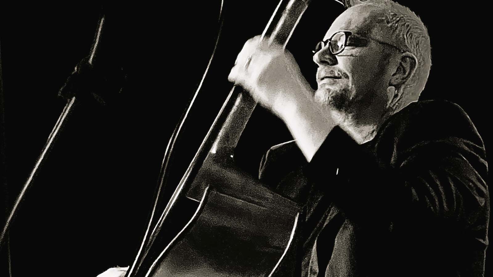 A musician passionately plays an upright bass on stage, captured in a dramatic black-and-white shot.