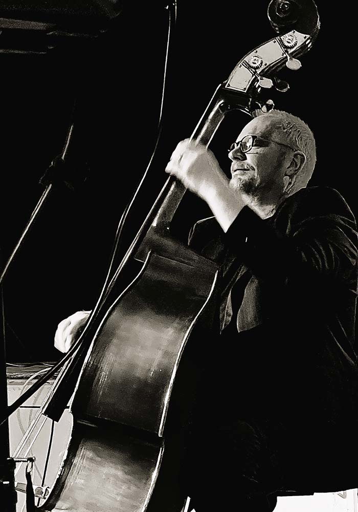 A musician passionately plays an upright bass on stage, captured in a dramatic black-and-white shot.