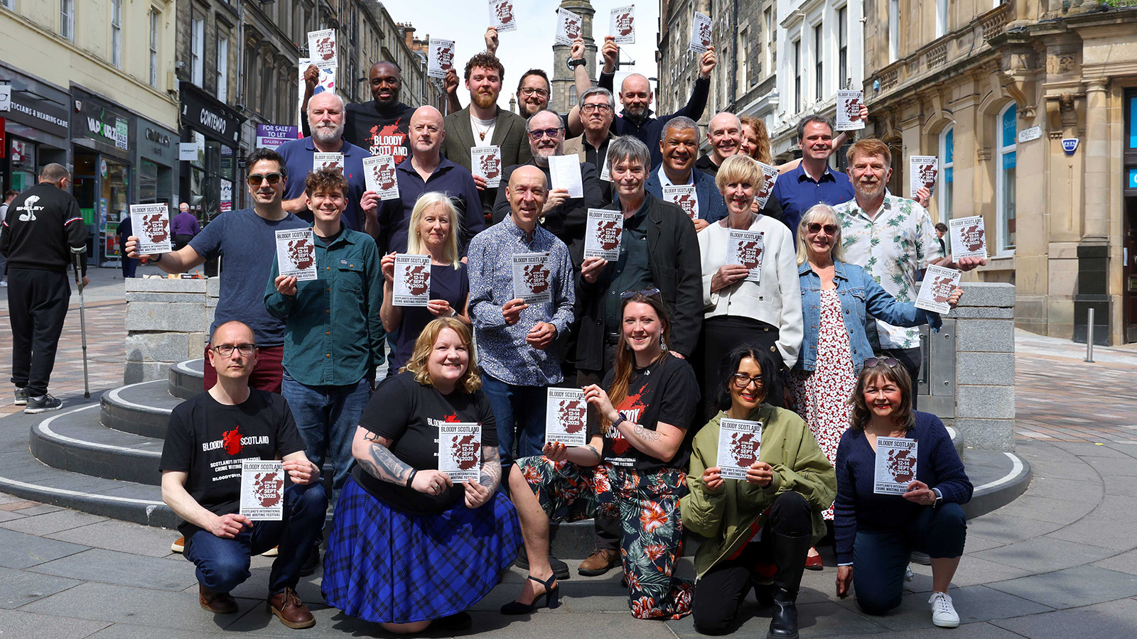 A diverse group of individuals gathers in a city square, holding event flyers for 