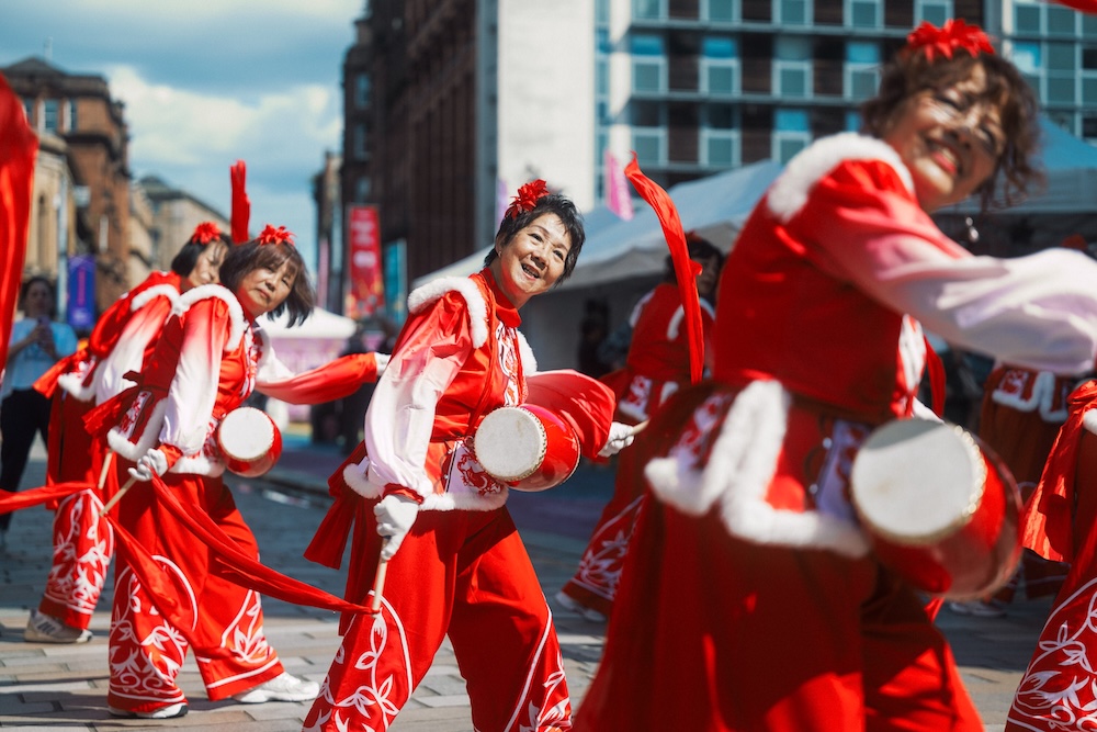 Performers in colourful red and white uniforms stand in Merchant City Glasgow