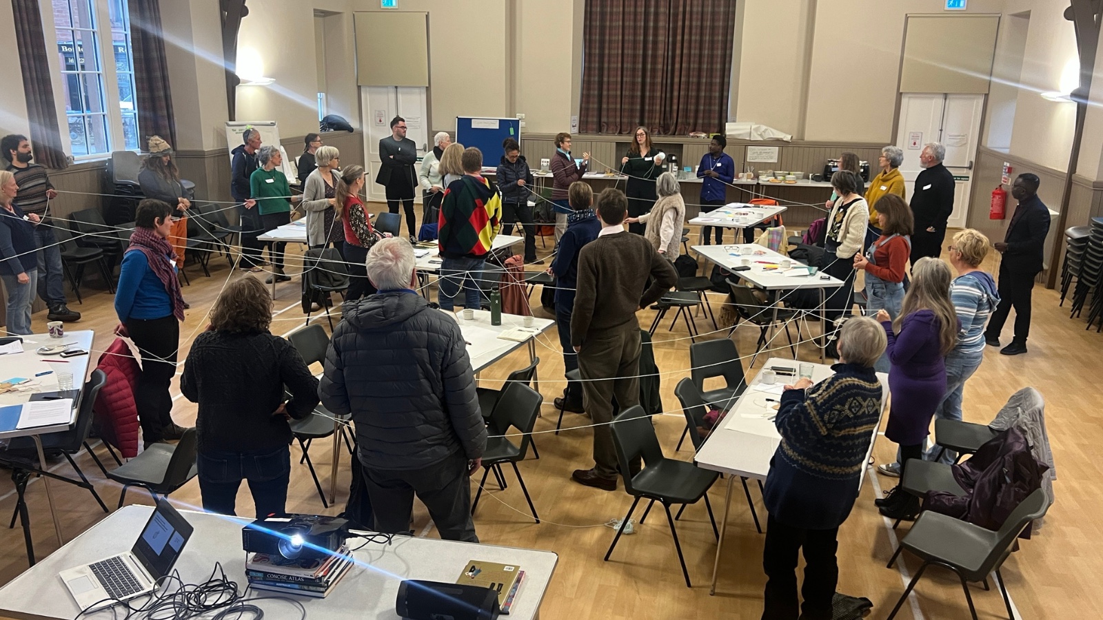 An image from a Culture for Climate Scotland event. A group of people are standing up from their tables and each hold string forming a web across the room.