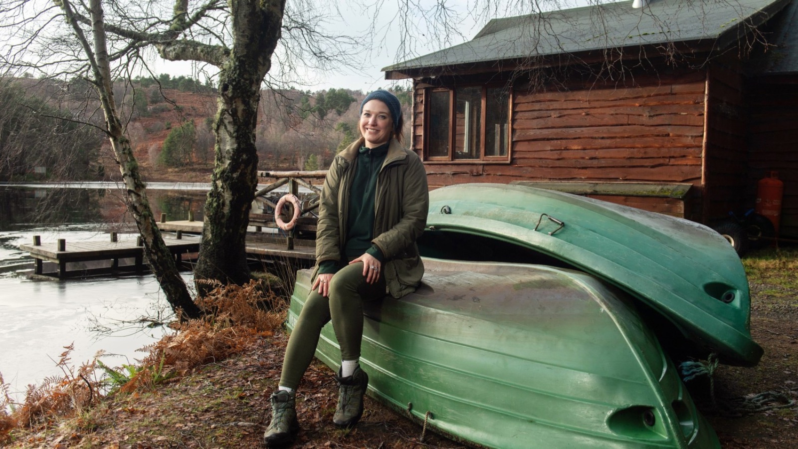An image of Lucy Holden on the shore of river, sat on two green boats.